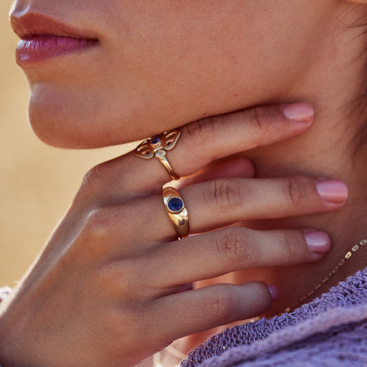 Mano de una mujer mostrando el anillo Simone, fabricado con oro de 18k y un zafiro azul natural en talla redonda.