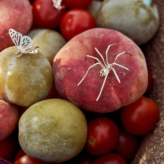 Pin Sipider, pin con forma de araña sobre un cesto de fruta. Muestra el detalle de esta joya fabricada en oro de 9k con dos rubíes naturales.